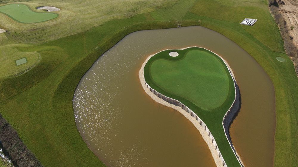 Huntsville Aerial view of a vibrant green synthetic grass island in a natural pond on a golf course